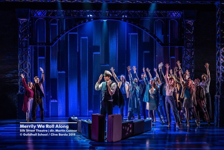 Actors in costume waving in a performance of Merrily We Roll Along